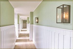 Høje, hvide paneler og stemningsskabende tapeter er et væsentligt element i indretningen af Strandhotellet. Her er det en af værelsesgang ene, hvor Le Corbusiers Dots-tapeter er det gennemgående element i naturfarverne: grøn, blå og solgul. Lampen er fra Møller & Rothe. Foto: Ulrik Bang/KASIK