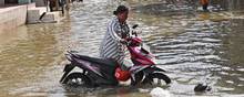 En kvinde trækker sin motorcykel gennem vandmasserne – forårsaget af en tidevandsbølge – i en gade i Indonesiens hovedstad, Jakarta, som er en af de hurtigst synkende byer i verden. Foto: Tatan Syuflana/AP