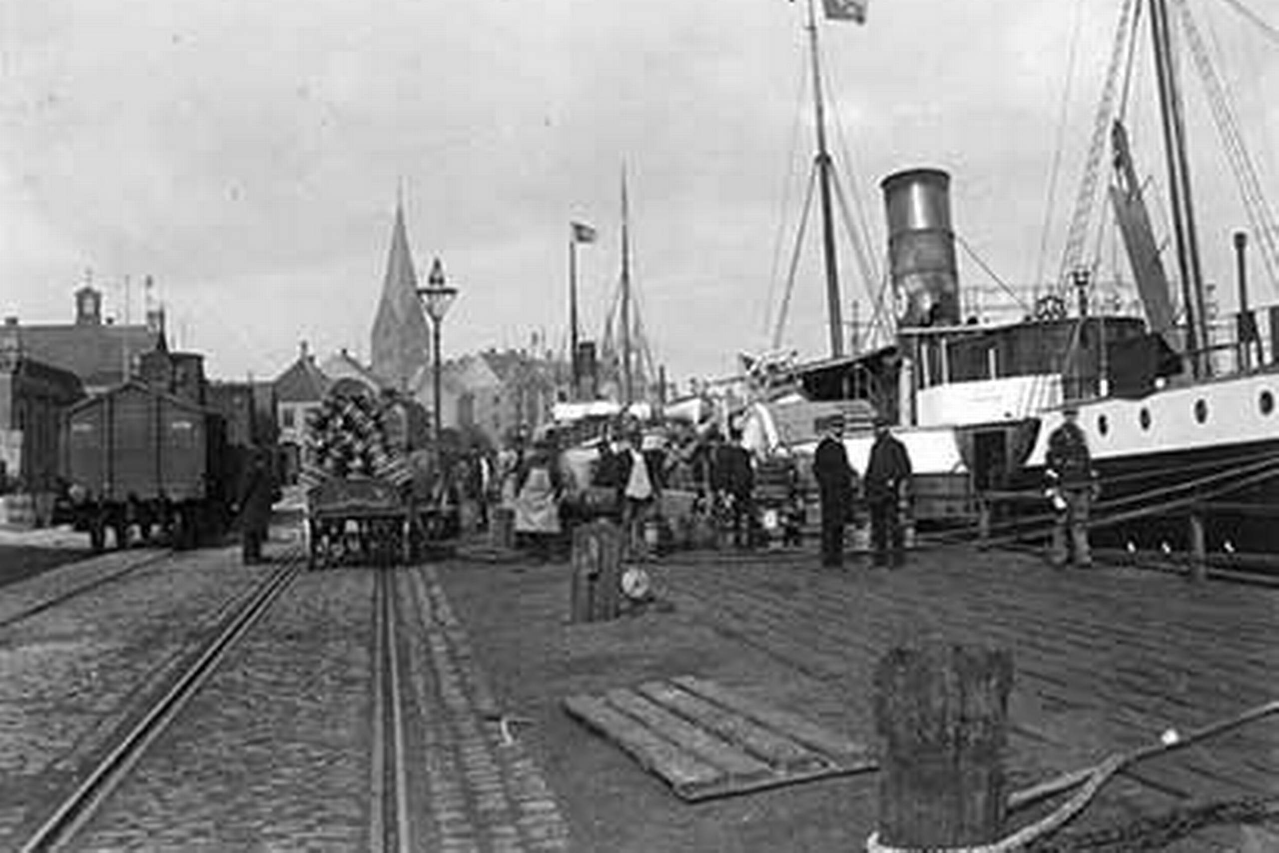Samspillet mellem havn og jernbane gav Aarhus gode vækstbetingelser. Byens erhvervsliv levede højt på at sende varer mellem havnen og dybt ind i det jyske bagland. På billedet fra omkring 1890 lastes et skib, der ligger ved Dampskibsbroen ud for den nu nedrevne varebørs. Det ser ud til at være smørdritler. Ukendt fotograf, Lokalhistorisk Samling, Aarhus
