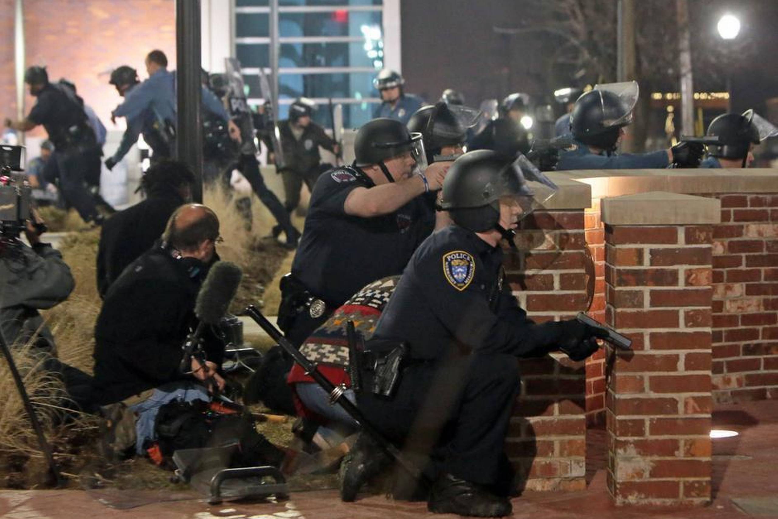 To betjente er netop blevet ramt af skud foran politistationen i Ferguson efter endnu en demonstration mod myndighederne. Skuddene faldt, timer efter at politichefen tog sin afsked. Ifølge politimester i St. Louis, Jon Belmar, er det et mirakel, at betjentene overlevede. Den ene blev ramt under øjet, hvorefter kuglen stoppede ved øret. Den anden blev ramt i skulderen. Foto St. Louis Post-Dispatch, Laurie Skrivan/AP.