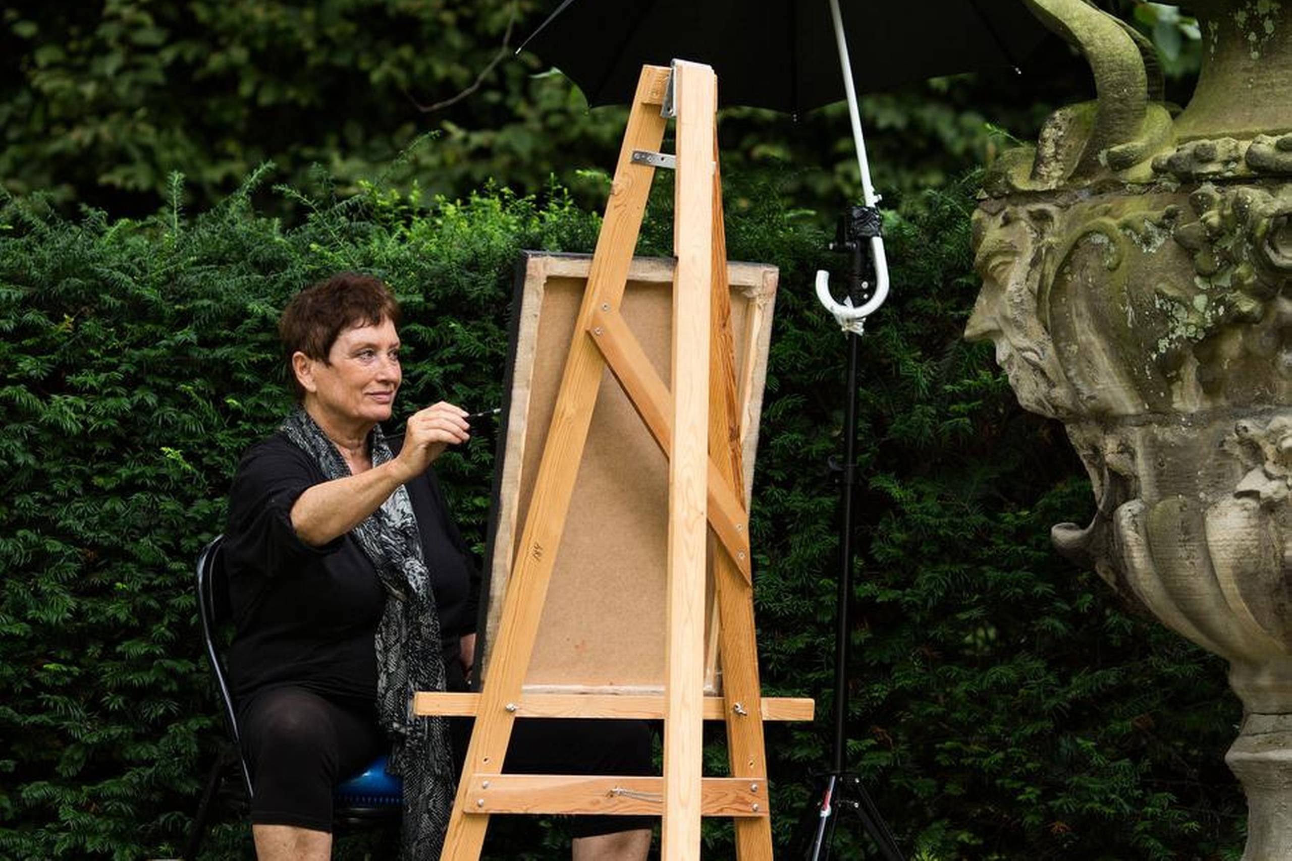 Pia Schutzmann maler i haven bag Christian 9.s Palæ, regentparrets residens på Amalienborg. Kunstneren er i færd med maleriet ”Faunen” med motiv fra den store vase. Paraplyen er et værktøj til at styre lysindfaldet på lærredet. Foto: Peter Nørby