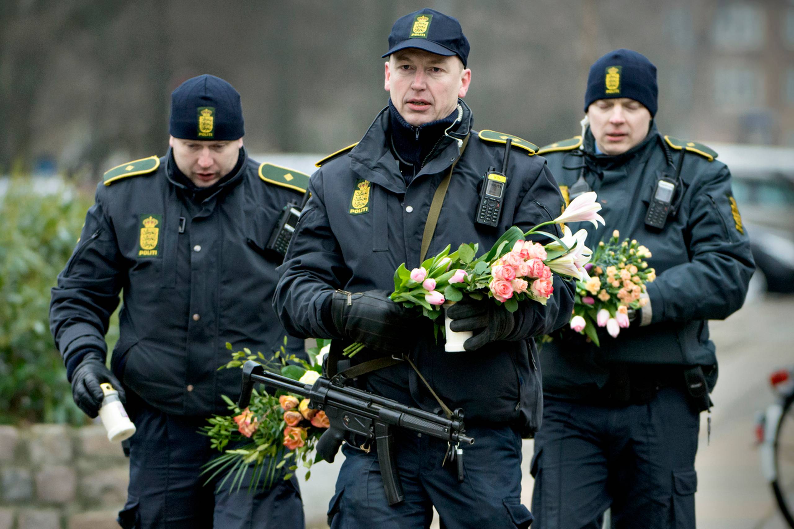Betjente bærer våben og flytter blomster til den hurtigt voksende bunke ved Krudttønden på Østerbro, hvor filminstruktøren Finn Nørgaard dagen før blev dræbt, og tre betjente såret, da Omar Abdel Hamid El-Hussein affyrede en byge af skud med maskinpistol under debatmødet med den svenske tegner Lars Vilks. Natten til søndag angreb attentatmanden endvidere den jødiske synagoge i Krystalgade i København, hvor vagtmanden Dan Uzan blev dræbt, og to betjente såret. Tekst og foto: Lars Krabbe 