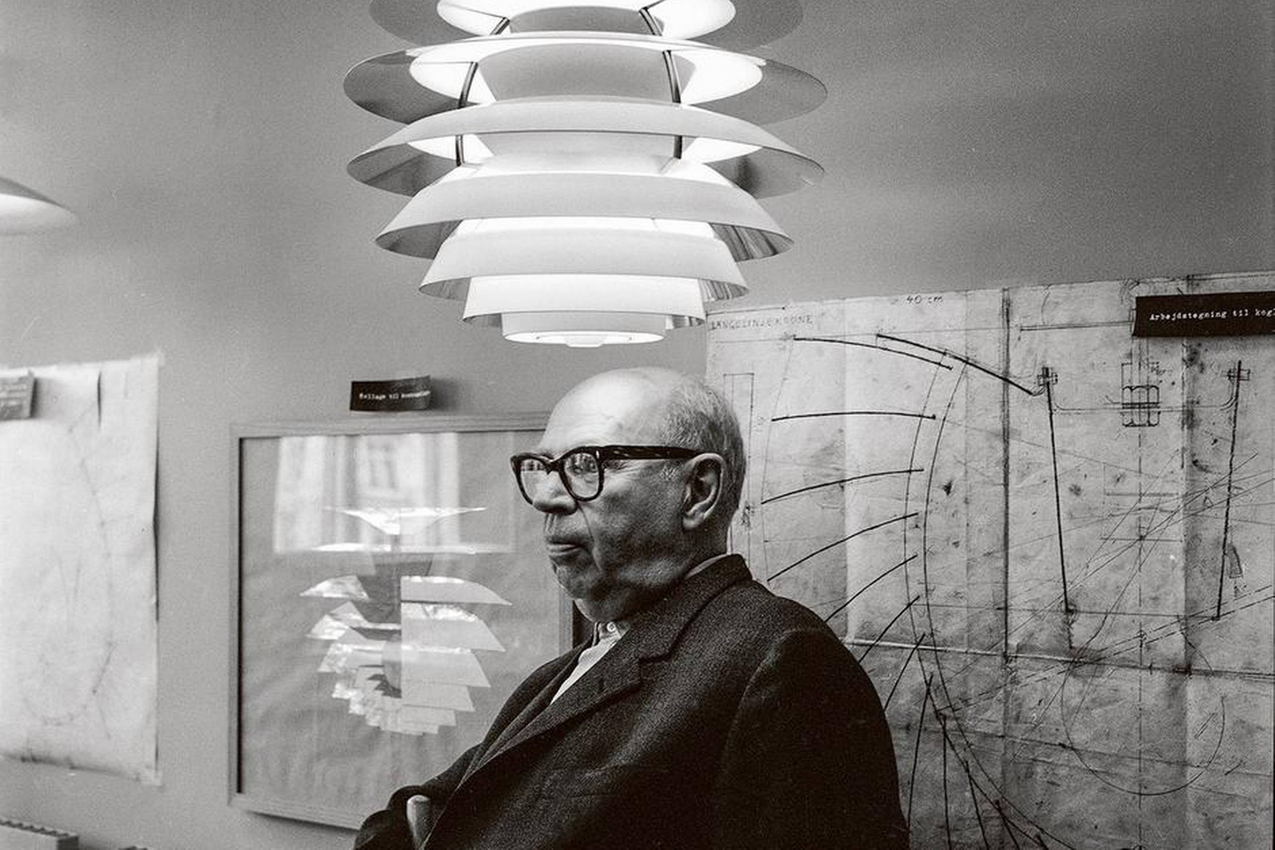 I 1964 fyldte Poul Henningsen 70. Dagen blev fejret med studenter i fakkeloptog og masser af festivitas. I Politiken kunne man læse et hyldestdigt af Klaus Rifbjerg (1931-2015), der betegnede PH som en »foregangsmand«, der var »rigtig underlig og underlig rigtig«. Billedet viser den 70-årige PH sammen med et par af hans mest udbredte lampetyper. Det stammer fra Louis Poulsens udstillingslokaler i Nyhavn, som bød på en særudstilling af ”lysmageren” PH og hans virke. Foto: Det Kongelige Bibliotek/Grethe Buhl