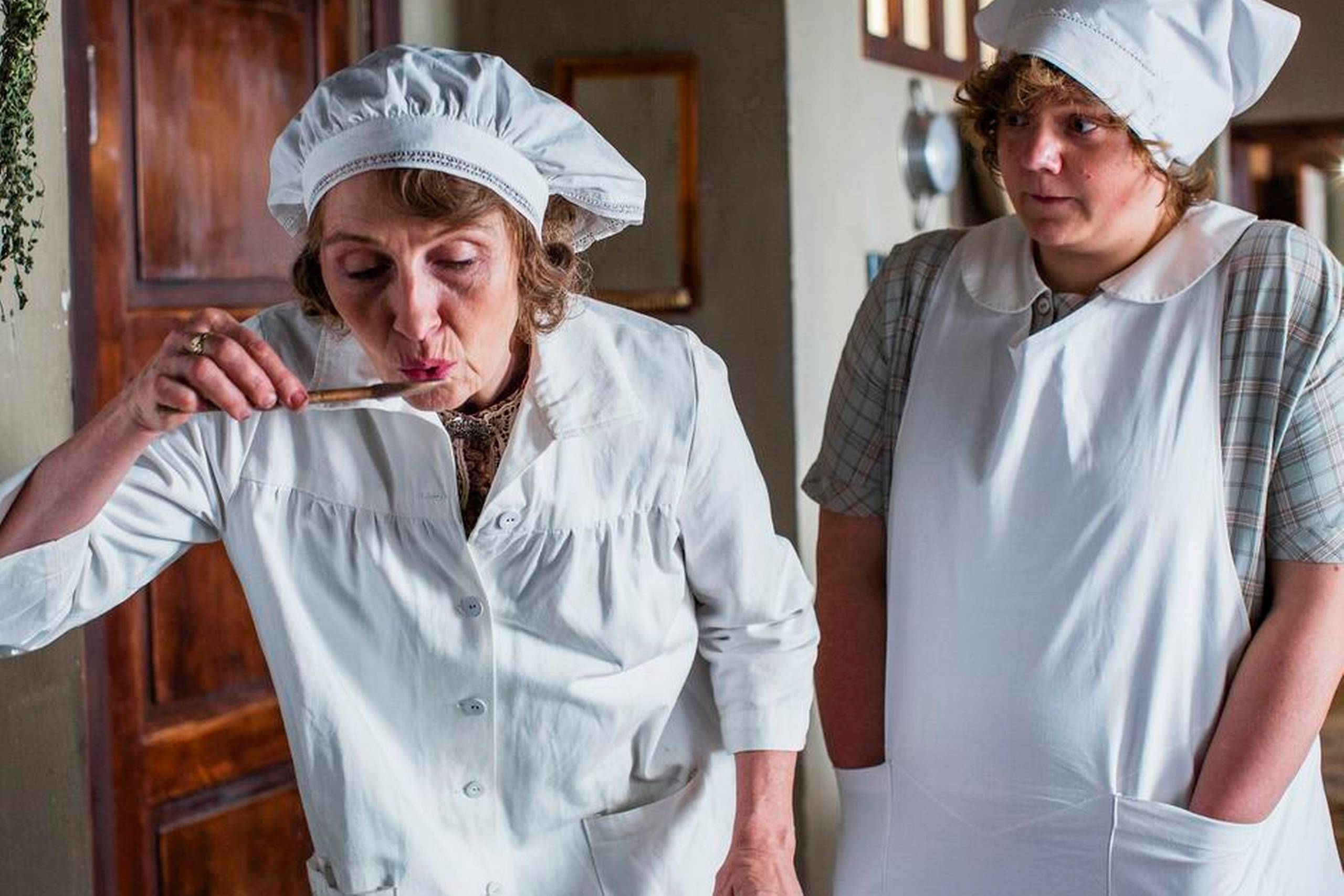 Bodil Jørgensen (t.v.) ses her i rollen som Molly Andersen, mens Ena Spottag står i baggrunden som kokkepigen Martha i tv-serien Badehotellet, der er en seermagnet på TV 2. Foto: Pr