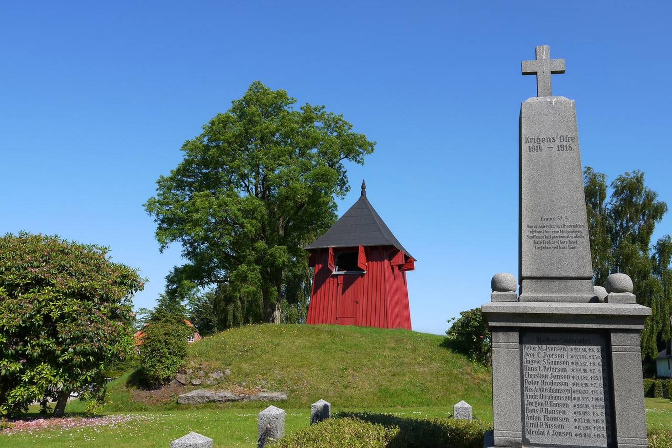 Bag mindesmærket for krigens ofre står Hjordkær Kirkes pyntelige klokketårn i træ. Foto: Arne Rudi Jensen