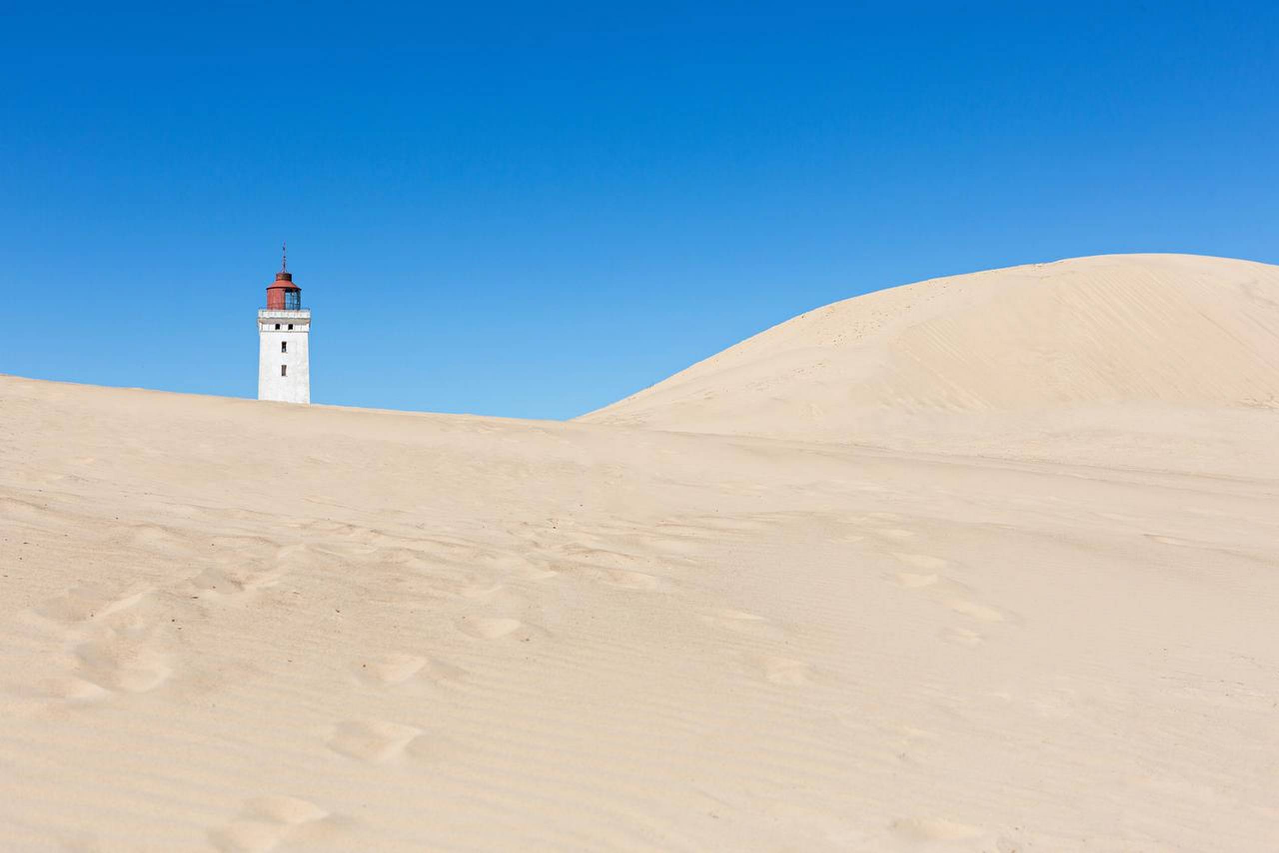 Det gamle fyrtårn ved Rubjerg Knude står tomt og ensomt ved den yderste skrænt mellem de enorme sandklitter. Foto: Getty Images